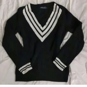 Svart och vit stickad tröja - Säljer en snygg svart stickad tröja med vita ränder vid v-ringningen och ärmsluten. Tröjan har en loose passform och är perfekt för höst och vinter. Den är långärmad och supermysig att ha på sig. Perfekt för en avslappnad stil eller att klä upp med accessoarer.