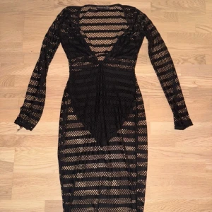 Svart nätklänning från PrettyLittleThing - Säljer en snygg svart nätklänning från PrettyLittleThing i storlek XS. Klänningen har en djup v-ringning och långa ärmar, perfekt för en utekväll eller fest. Den är i mycket bra skick och ger en cool och edgy look. Passar perfekt över en enkel underklänning eller bikini.