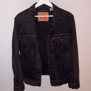 Svart jeansjacka från Levi's - Snygg svart jeansjacka från Levi's med klassisk design. Jackan har knappar framtill och två bröstfickor med knappstängning. Perfekt för en avslappnad stil. Nypris ca 1300kr