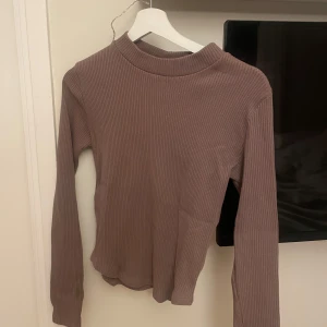 Brun ribbad långärmad tröja - Säljer en stilren brun ribbad tröja med långa ärmar. Enkel att matcha med olika outfits och säljs inte längre i butik. Bra meterial.