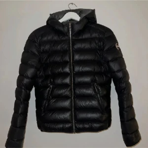 Svart dunjacka från colmar  - Snygg svart dunjacka från colmar med huva och dragkedja. Perfekt för kyliga dagar med sin vadderade design. Jackan har en stilren look och är både funktionell och trendig.