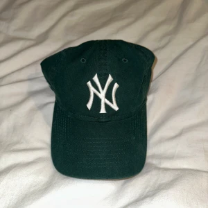 Grön keps från Aimé Leon Dore - Snygg grön keps med vit broderad logga framtill och Aimé Leon Dore-text på sidan. Perfekt för en casual look. Justerbar passform för optimal komfort. Senaste pris på StockX för denna keps var på 360 dollar