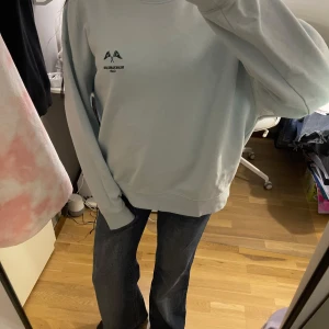 Ljusblå sweatshirt från H&M - Säljer en jättefin ljusblå sweatshirt från H&M med tryck på bröstet. Tröjan har långa ärmar och ribbade muddar vid ärmslut och nederkant. Perfekt för en avslappnad look.