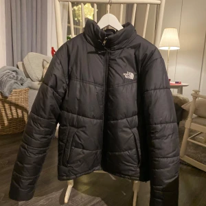 Svart dunjacka från The North Face - Säljer en svart dunjacka från The North Face. Jackan är 1 år gammal om ganska använd men fortfarande bra skick utan deffekter.  Storlek S och passar från 160cm-175cm uppskattar jag. Perfekt nu för vintern!    Skriv om ni har frågor. Friset är inte hugget i sten/ elis   