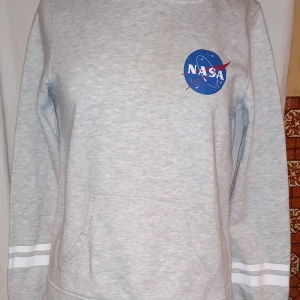 Grå NASA hoodie från H&M - Säljer en grå hoodie från H&M med NASA-logga på bröstet och ryggen. Tröjan har långa ärmar och en praktisk magficka. Perfekt för alla rymdentusiaster! 🚀