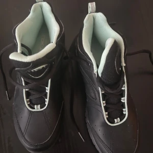 Svarta sneakers från Reebok - Snygga svarta sneakers från Reebok med mintgröna detaljer och snörning. Perfekta för en sportig look eller vardagsbruk. Skorna har en robust sula för extra komfort.