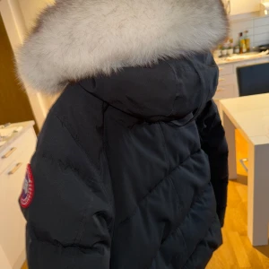 Canada Goose / Silver räv päls - Säljer en svart dunjacka från Canada Goose med en lyxig pälsdetalj på huvan. Jackan har en klassisk pufferdesign med långa ärmar och en praktisk dragkedja framtill. Perfekt för kalla vinterdagar.