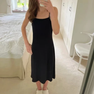 Svart klänning - Elegant svart klänning med smala axelband och enkel design. Perfekt för en stilren look.