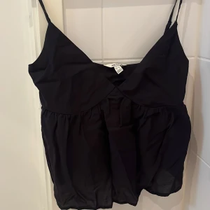 Svart linnetopp från vero Moda - Snygg svart linnetopp från vero moda med smala axelband och v-ringning. Perfekt för varma dagar eller under en kofta. Enkel och stilren design som passar till många olika outfits.