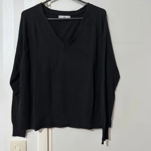 Svart tröja från MNG - Säljer en stilren svart tröja från MNG med v-ringning. Tröjan har långa ärmar och en ribbad kant vid nederdelen. Perfekt för en minimalistisk look.