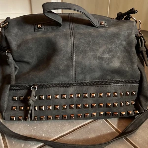 Rockig väska med nitar! - Snygg rockig väska med nitar i svart mocka med både handtag och avtagbar axelrem. Mått: 25 x 30 cm. Oanvänd.