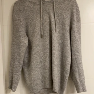 Grå kashmirer hoodie - Mysig grå kashmir hoodie med långa ärmar och justerbar huva från sayless. Perfekt för kyliga dagar med sin mjuka och bekväma passform. Ribbstickade muddar vid ärmslut och nederkant ger en stilren look. Skick 9/10. Vid fler frågor eller funderingar så skriv 👌