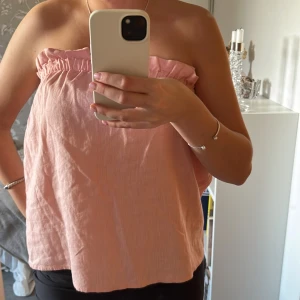 Rosa axelbandslös topp - Säljer en söt rosa axelbandslös topp med volangdetalj vid kanten. Perfekt för varma sommardagar.