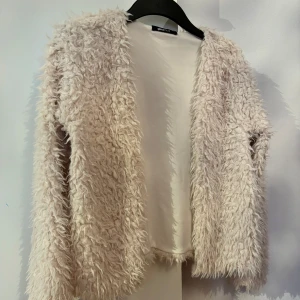 Vit Teddykofta från Gina Tricot - . Perfekt för kyliga dagar med sin fluffiga och mjuka textur. Koftan har en öppen design utan knappar eller dragkedja, vilket ger en avslappnad look.