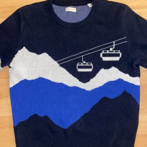 Mörkblå stickad tröja med bergsmotiv från GANT - Säljer en snygg mörkblå stickad tröja från GANT med ett coolt bergsmotiv i vitt och blått. Tröjan har långa ärmar och en rund halsringning. Perfekt för kyliga dagar!
