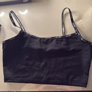 Svart linnetopp från Levi's - Snygg svart linnetopp från Levi's med smala axelband och logotyp längs kanterna. Perfekt för en avslappnad stil eller som lager under andra plagg.
