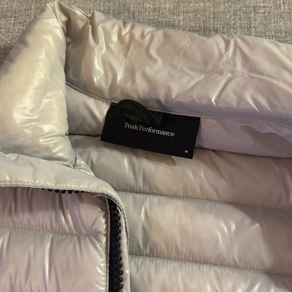 Snygg och stilren grå pufferjacka från Peak Performance. Jackan har en dragkedja framtill och praktiska fickor med dragkedjor. Perfekt för kyligare dagar med sin quiltade design.. Takit.