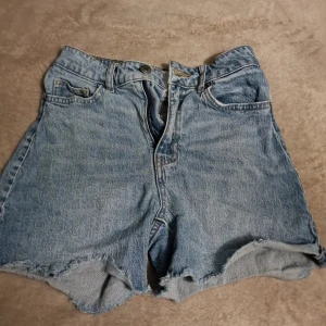 Blå jeansshorts från H&M - Säljer ett par klassiska blå jeansshorts från H&M. De har en avslappnad passform med fransiga kanter och femficksdesign. Perfekta för en avslappnad stil.