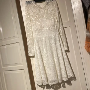 Bal.Fest.Bröllop  - Elegant vit spetsklänning från SisterS Point med långärmad design och vackert blommönster. Klänningen har en klassisk passform och är perfekt för speciella tillfällen.