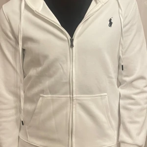 Vit huvtröja från Ralph Lauren - Snygg vit huvtröja från Ralph Lauren med dragkedja och broderad logga på bröstet. Tröjan har långa ärmar och en praktisk huva. Perfekt för en avslappnad stil. Jag säljer den då den också blivit liten på mig. Ingen skada alls. Pris kan diskuteras 