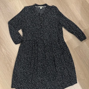 Svart och vit prickig klänning från Esprit - Snygg och bekväm svart klänning från Esprit med vita prickar och knappar framtill. Klänningen har långa ärmar och en bekväm passform som passar perfekt för både vardag och speciella tillfällen.