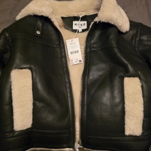 Svart jacka med foder från NA-KD - Snygg svart jacka från NA-KD med mysigt foder. Jackan har en dragkedja framtill och en klassisk design. Perfekt för kyligare dagar. Endast provad och lapparna sitter kvar.