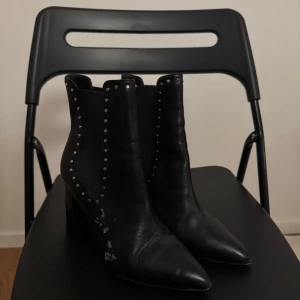 Svarta boots med nitar - Snygga svarta boots med spetsig tå och dekorativa nitar längs sidorna. Perfekta för en edgy look.Lite söndriga på sidan som man ser på bild men kan förmodligen tas bort om man tvättar eller nåt.
