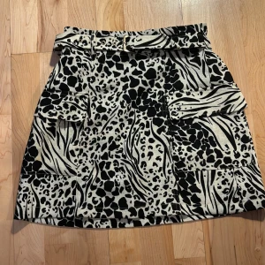 Mönstrad kjol från River Island.  - Snygg kjol från River Island med ett trendigt leopard- och zebramönster i svart och beige. Kjolen har ett matchande bälte som ger en extra touch. Perfekta kjolen för att ge outfiten en extra touch. Tror verkligen denna kjol passar äldre än 10 år, då den är ganska lång (40cm) men har en ganska tajt midja. Kvaliten är även mycket bra! Aldrig använd!