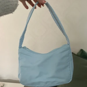 Ljusblå axelväska från Gina Tricot - Snygg ljusblå axelväska från Gina Tricot med dragkedja, enkel och stilren design. Använd 2 gånger men har två små fläckar, men de syns knappt. 