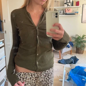 Olivgrön kofta - Säljer en olivgrön kofta med knappar framtill. Den har långa ärmar och en klassisk design som passar perfekt för höst och vår. Perfekt för att lägga till en touch av färg till din garderob.