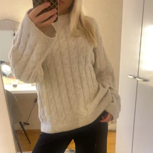 Beige stickad tröja från H&M - Mysig beige stickad tröja från H&M med kabelstickat mönster. Tröjan har långa ärmar och en rund halsringning, perfekt för kyligare dagar. Passar bra till både jeans och kjol.