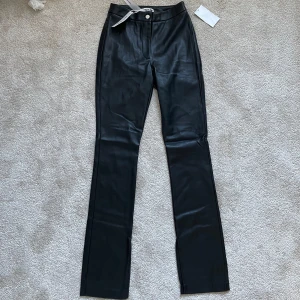 Svarta skinnbyxor storlek 38 - Snygga svarta skinnbyxor med hög midja och bootcut-stil. Perfekta för en trendig look med en dragkedja och knapp framtill.