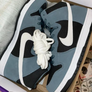 Nike SB Dunk High Pro Mineral Slate - Snygga Nike SB Dunk High Pro i färgen Mineral Slate med vita detaljer. Skorna har en hög design med snörning och en robust sula. Perfekta för både stil och komfort.