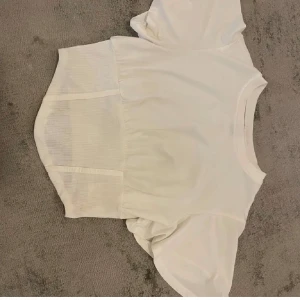 Vit ribbad topp - Säljer en vit ribbad topp med korta ärmar och en tight passform. Toppen har en elastisk midja som ger en smickrande silhuett som framhäver kurvorna då den snyggt blir tight vid midjan, storlek S —> passar XS