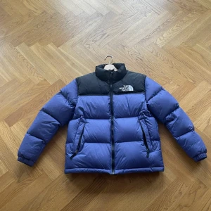 Lila och svart dunjacka från The North Face - Säljer en lila och svart dunjacka från The North Face. Jackan har en dragkedja framtill och är perfekt för kalla dagar. Den är långärmad och har en hög krage för extra värme.