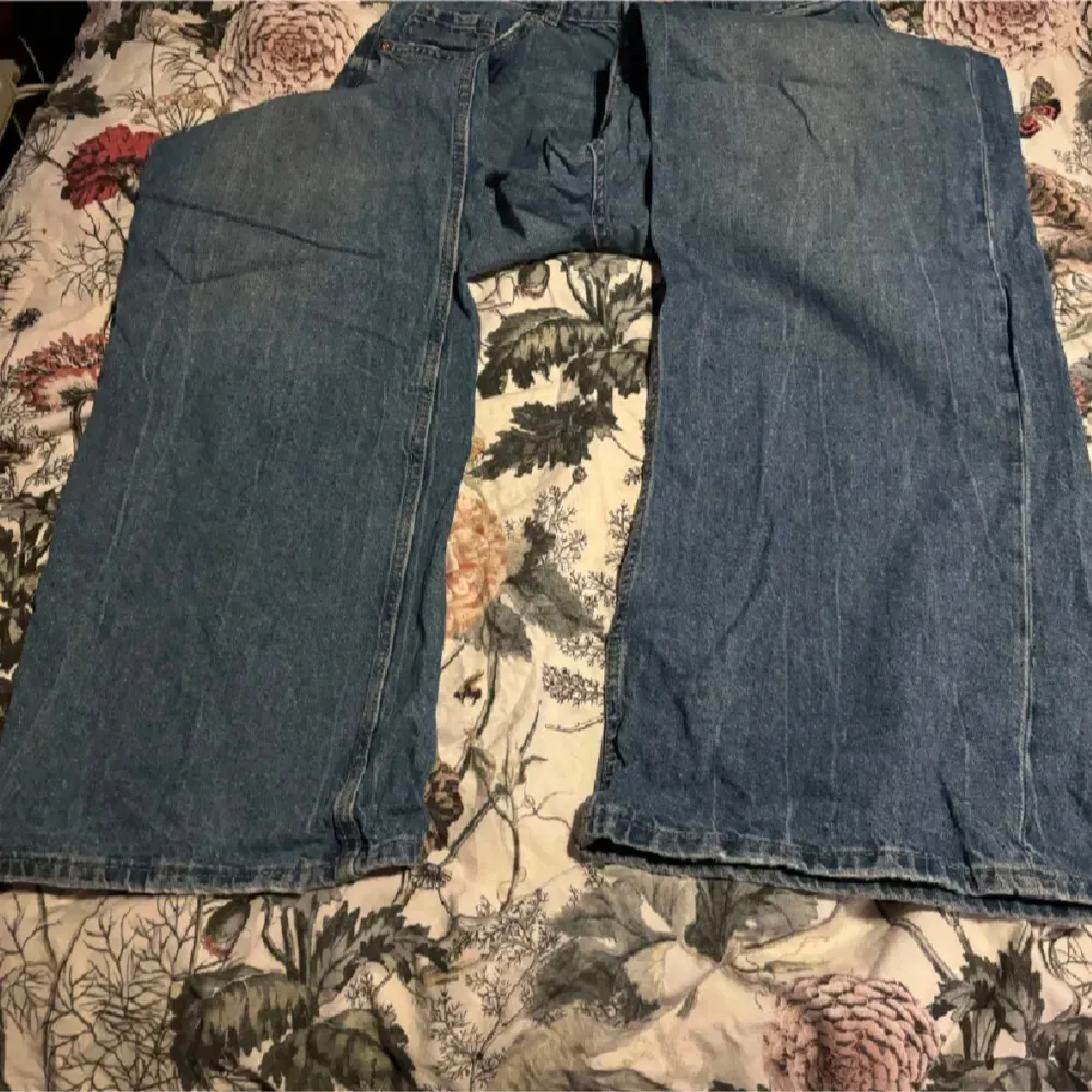 Säljer ett par klassiska blå jeans med hög midja och breda ben. De har en traditionell femficksdesign och stängs med dragkedja och knapp. Perfekta för en avslappnad stil.. Farkut & Housut.