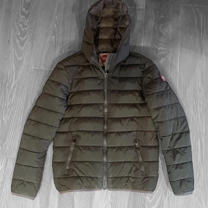 Grön pufferjacka med huva -  Till salu: Mörkgrön Dunjacka från Colmar – Stil och Funktion i Perfekt Kombination!  Är du på jakt efter den perfekta jackan för kalla dagar? Då är denna eleganta dunjacka från Colmar precis vad du behöver!   - Premium Kvalitet: Tillverkad av högkvalitativa material som ger både värme och komfort.          Priset kan diskuteras vid en snabb affär! 