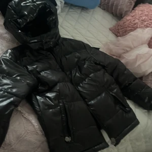 Moncler/fashion jacka  - Snygg svart glansig dunjacka från Moncler med huva och dragkedja. Jackan har långa ärmar och praktiska fickor med dragkedjor. Perfekt för kyliga dagar. Den är helt ny men den passa inte mig och vill sälja den 
