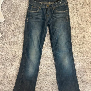 Blå jeans från Cross Jeanswear Co. - Snygga blå jeans från Cross Jeanswear Co. med klassisk femficksdesign och subtila slitningar. De har en normal passform och är perfekta för en avslappnad stil. Märkeslogga på baksidan ger en extra touch.