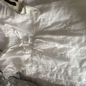 Vit klänning med spetsdetaljer - Säljer en superfin vit klänning med vackra spetsdetaljer och broderier. Den har en söt rosett i midjan och volanger vid ärmarna. Perfekt för sommarens alla fester eller kanske till midsommar! 💫