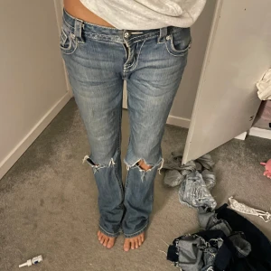 Blå jeans med slitningar - MISS ME blå jeans med coola slitningar på knäna. låg midja och en bootcut passform. Jeansen har snygga detaljer med knappar och fickor bak.midje mått ca : 40 men strechiga. innerbenslängd: ca 79. igensytt hål vid skrevet så tänk på d innan ni köper