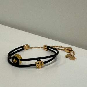 Kira Bracelet är inspirerad av retro vänskapsstilar. Man kan justera skjutreglaget för att få en perfekt passform.  - Läder, 18k guldpläterad mässing, slipad emalj - Justerbart skjutreglage - Nickelfri