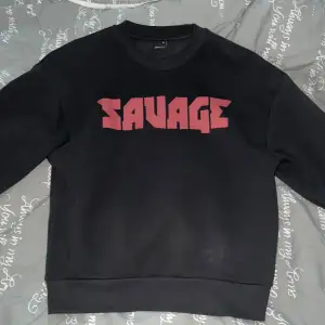 Säljer en cool svart sweatshirt från Gina Tricot med texten 'SAVAGE' i rött på framsidan. Tröjan är i storlek XS och har en normal passform. Perfekt för en avslappnad stil eller att mysa i hemma. Den är i bra skick och superbekväm!