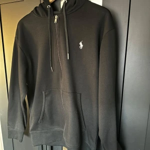 Svart hoodie från Ralph Lauren - Säljer en stilren svart hoodie från Ralph Lauren. Den är i väldigt bra skick. Den passar dig som är runt omkring 180cm lång och har en hyfsat smal passform. 