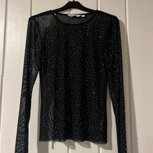 Svart glittrig meshtröja - Säljer en svart meshtröja med glittriga detaljer. Den är långärmad och perfekt för festliga tillfällen. Tröjan är genomskinlig och har en tight passform som ger en snygg siluett. Perfekt för att lägga till lite bling till din outfit! ✨