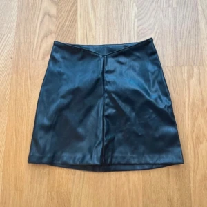 Svart kjol i skinnimitation - Snygg svart kortkjol i skinnimitation med en stilren design. Kjolen har en diskret dragkedja på sidan och en lätt A-linjeformad passform. Storlek XXS från h&m