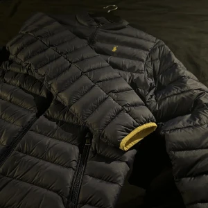 Ralph lauren jacka - Snygg svart dunjacka från Ralph Lauren med dragkedja och broderad logotyp på bröstet. Jackan har en quiltad design och långa ärmar, perfekt för kyligare väder. Storleken är 170/xxs.(Köpt för 2499 säljer för 899)