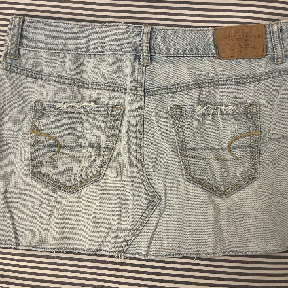 Säljer en snygg ljusblå jeanskjol från American Eagle. Den har en cool distressed look med slitningar och en korsad design framtill 💘 Står storlek 4 (USA), upplever den som en XS/S. . Kjolar.