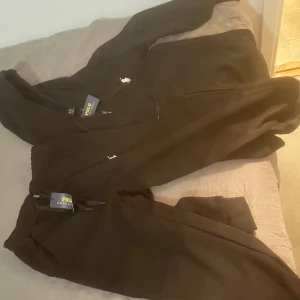 Svart tracksuit från Polo Ralph Lauren - Säljer en svart tracksuit från Polo Ralph Lauren i nytt skick. Setet består av en hoodie och byxor, båda med märkets ikoniska logga. Perfekt för en avslappnad stil eller träning. Storleken är herr m och materialet känns mjukt och bekvämt. Köpt är köpt tar ej tbx 