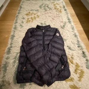 Svart dunjacka från Moncler - Säljer en snygg svart dunjacka från Moncler i mycket bra skick. Jackan har en dragkedja framtill och två praktiska fickor med dragkedjor. Perfekt för kyliga höst- och vinterdagar. Den är både stilren och varm, vilket gör den till ett måste i garderoben!. Tar också emot byten